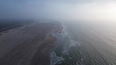 Göz kamaştırıcı bir hava görüntüsü sisli bir kıyı şeridini yakalıyor. Yumuşak dalgalarla birlikte sahilde hafifçe tur atıyor.