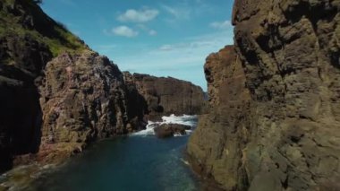 Parlak mavi gökyüzünün altındaki sakin suların yanında kayalık kayalıkları gösteren nefes kesici bir kıyı manzarası.