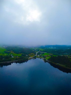 Havadan güzel bir manzara, kıvrımlı yollar boyunca yemyeşil tepelerle çevrili dingin, sisli bir gölü yakalar.
