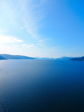 Güzel bir gölün sakin ve sakin bir manzarası görkemli dağlarla çevrili, üzerinde çarpıcı mavi bir gökyüzü var.