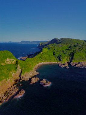 Bereketli yeşil tepeler ve sakin suların bulunduğu nefes kesici bir kıyı şeridi manzarası.