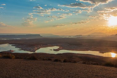 Colorado Nehri, Glen Canyon Barajı 'na yaklaşıyor güneş doğarken dağların ve nehrin üzerinde güzel bir altın parıltı ve bulutlarla dolu renkli bir gökyüzü yaratıyor.. 