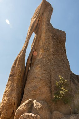 ABD 'nin Güney Dakota eyaletinin Black Hills bölgesindeki Custer State Park' taki Needles Otobanı 'ndaki Needles Eye kaya oluşumuna yakın çekim. Güneş lekeleri olan parlak mavi bir gökyüzü. Resim dikey.