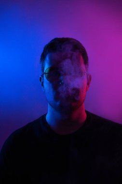 Neon renklerin büyüleyici bir kombinasyonuyla, bir adam sigara içerken etrafındaki dumanları büyülüyor, büyüleyici bir atmosfer yaratıyor.