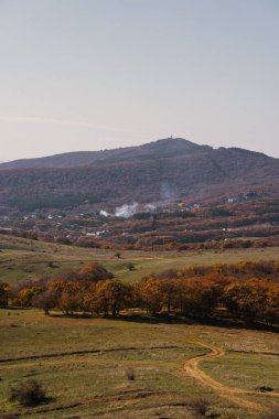 Yuvarlanan tepeler, yakındaki bir köyden yükselen dumanla uzaktaki görkemli dağlara karşı canlı sonbahar renklerini sergiliyor..