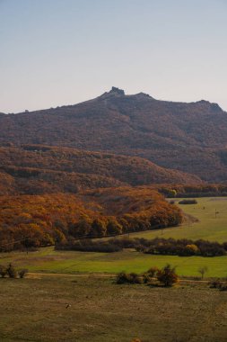 Sonbahar yapraklarının canlı renkleri açık gökyüzünün altındaki tepeleri ve vadileri kaplıyor, doğanın güzelliğini vurguluyor..