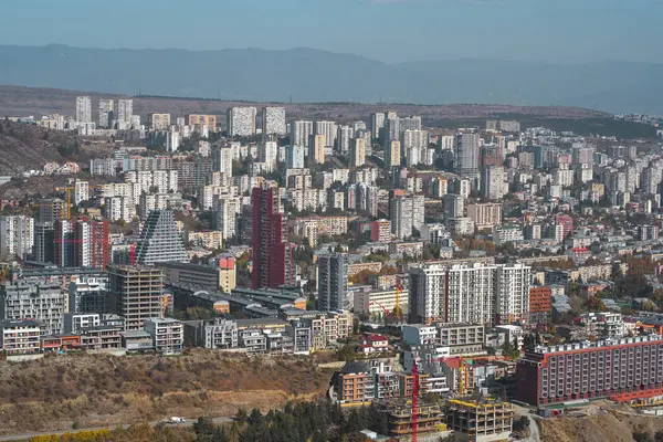 Şehir siluetinde açık mavi gökyüzü altında modern binalar ve devam eden inşaat projelerinin bir karışımı yer alıyor..