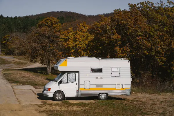 Klasik bir karavan, canlı sonbahar ağaçları ve dolambaçlı bir yol ile çevrili beton bir yüzeyde duruyor..