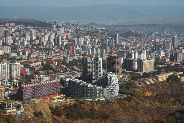 Parlak şehir hayatı, sonbaharda berrak bir gökyüzünün altında kayan tepelerin önünde yükselen binalar gibi gözler önüne seriliyor..