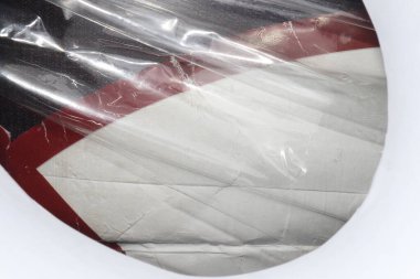 A close-up of a white and red object wrapped in transparent plastic. The object has a circular shape and a smooth texture.  clipart