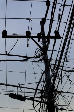 Elektrik kablolarının karışıklığı gri gökyüzüne karşı elektrik direğini kaplıyor..