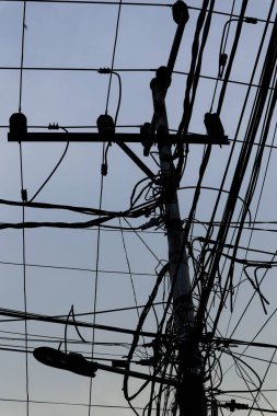 A tangled mess of electrical wires covers a utility pole against a gray sky. clipart