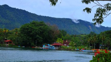 Danau Toba, 09 Kasım 2024 - Geleneksel Batak evleri yemyeşil dağlarla çevrili sakin bir göl kıyısında. Sumatra Utara, Endonezya.