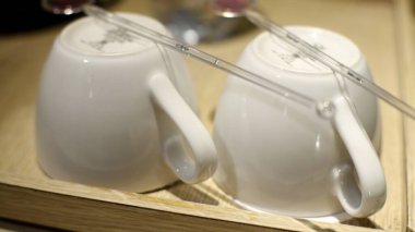 Two white coffee cups with stirrers are placed upside down on a wooden tray. clipart