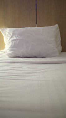 Görüntü minimalist yatak odasını gösteriyor. Yatağın üzerinde beyaz bir yastık var..