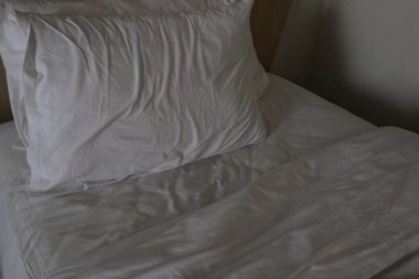 Kırışık beyaz bir yatak örtüsü hafifçe geri çekilir ve yumuşak beyaz bir yastık ortaya çıkar..