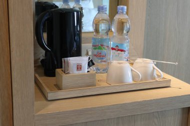 Pekanbaru, 21 Kasım 2024 içinde siyah bir elektrikli su ısıtıcısı, iki şişe maden suyu, birkaç paket çay ve kahve, iki beyaz kahve fincanı ve bir karıştırıcı bulunan ahşap bir tepsi. Riau, Endonezya.