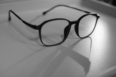 A pair of black framed glasses with clear lenses is placed on a white surface. clipart