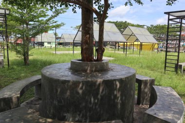  Parkta bir ağacı çevreleyen beton bir bank.