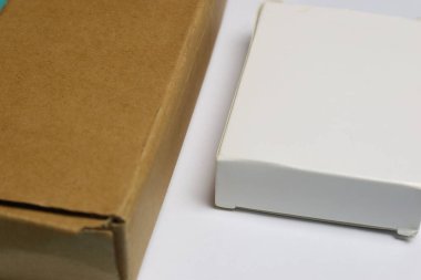 Beyaz bir yüzey üzerinde beyaz bir kutu ve kahverengi bir kutu yan yana yerleştirilir..