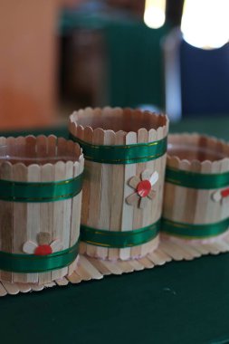 Yeşil kurdele ve çiçek aksanıyla dekore edilmiş üç küçük el yapımı ahşap kap. Bu el sanatları bulanık bir arkaplan üzerine kuruludur, onların sanatsal niteliklerini ve karmaşık detaylarını vurgular..