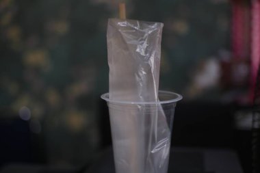 Plastik bardağın içindeki buruşuk plastik poşetin yakın plan görüntüsü, tek kullanımlık plastik ve atık imhası ile ilgili çevre sorunlarını vurguluyor.