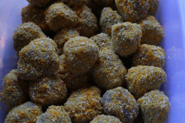 Yakın plan çekimde, tamamen çıtır çıtır, altın rengi ekmek kırıntılarıyla kaplı sayısız küçük yuvarlak şekerlemeler ortaya çıkıyor. Net bir plastik konteynırın içine yerleştirilmişler..