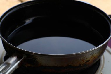 Yakından bakınca koyu bir sıvı, muhtemelen yağ, iyi kullanılmış metal bir tavada. Tavada yaş ve kullanım belirtileri gösterilir ve resme rustik kalite eklenir.