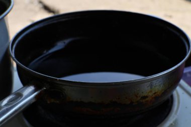 Koyu sıvı içeren eski metal bir tavaya yakından bakın. Geniş kullanım ve hafif renk bozulması belirtileri gösteriyor. Görüntü dokuyu ve kırsal detayları vurgular.