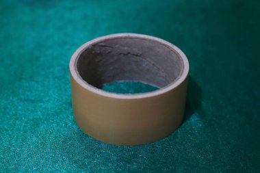 Detaylı bir yakın plan çekimde bir rulo bej yapışkan bant görünür, bir deniz mavisi kumaşı yüzeyinde durur. Görüntü hem bandın hem de kumaşın dokusunu vurgular.