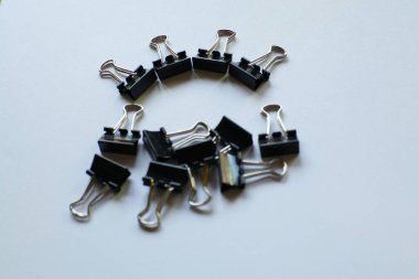 Bir grup siyah klasör klipleri beyaz bir arkaplan üzerinde düzenlenmiş, bazıları eğri bir çizgi üzerinde, iş ve eğitim temaları için minimalist ve organize bir kompozisyon oluşturur.