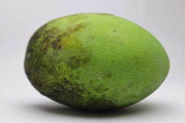 Olgunlaşmamış yeşil bir mangonun beyaz yüzey arka planında lekeler olan yakın plan çekimi..