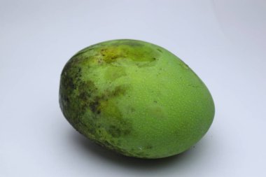 Beyaz arka planda olgunlaşmamış yeşil bir mango meyvesinin yakın çekimi. Canlı rengini ve taze, doğal dokusunu vurguluyor.