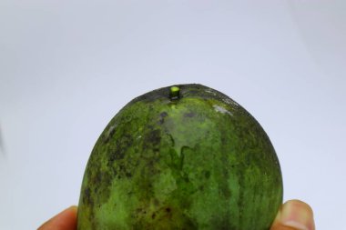 Yakından çekilen bir fotoğraf olgun olmayan bir mangonun canlı yeşil ve dokulu derisini yakalar. Bir elde tutulan meyve parlak, nötr bir arkaplana karşı sergilenir, doğal kusurlarını ve taze görünümünü vurgular. Bu görüntü mükemmel olur.