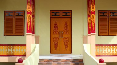 Ayrıntılı ön cephede, geleneksel mimari stil ve canlı renklerin yer aldığı ahşap kapılar ve pencereler yer alıyor..