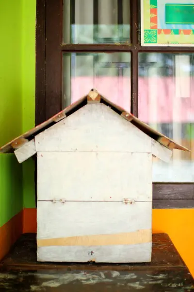 Kırsal, el yapımı, minyatür ahşap bir ev renkli bir duvara ve eski pencere çerçevesine dayanır. Basit bir yapı ve eski dokuları sergiler..