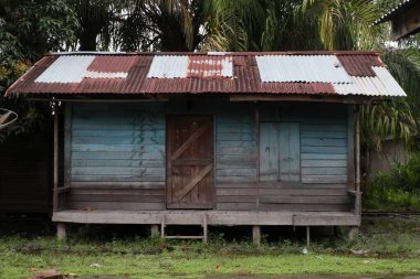 Oluklu demir çatılı eski ahşap bir ev tropikal bir ortamda eskimiş bir cazibe sergiliyor..