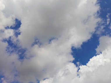 Güzel mavi bir gökyüzü yumuşak, dalgalı beyaz bulutlarla çelişiyor. Atmosferik manzara, aydınlık bir yaz gününde huzur ve sükunet hissi uyandırır..