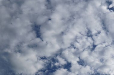 Uçsuz bucaksız, tüylü, yumuşak kümülüs bulutlarıyla kaplı gökyüzü açık mavi bir zemin üzerinde.