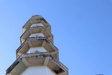 Açısal katmanlı bir kule, açık mavi gökyüzüne doğru yükselir ve basit ve geometrik bir şekil verir..