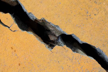 Sert bir makro çekim sarı beton bir alanda önemli bir yırtık olduğunu gösteriyor. Çatlak, maddenin kırılganlığını ve ayrışmasını vurgulayan koyu bir boşluğu ortaya çıkarıyor.