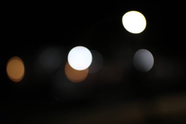 Bokeh ışıklarının derin, siyah bir arkaplana karşı sanatsal bir gösterimi, çarpıcı, görsel olarak çekici, ruhani bir güzellikle soyut bir görüntü yaratıyor.