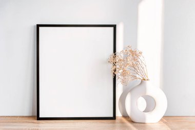 Boş bir çerçeve ve ahşap bir yüzey üzerindeki zarif bir vazoda kurumuş çiçekleri barındıran minimalist iç dekorasyon.