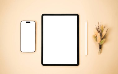Temiz bir çalışma alanında akıllı bir telefon, tablet ve stil, bir buket kurumuş çiçeğin yanında, nötr tonlu bir ortamda üretkenlik için sakin bir atmosfer oluşturur..