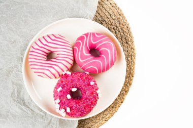 Üç lezzetli çörek yuvarlak bir tabakta, canlı pembe kremalar ve renkli serpiştirmeler sergiliyor. Kutlama, tatlı masası ya da toplantı sırasında atıştırmak için ideal bir yer..