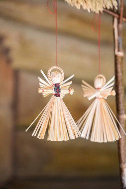 Doğal ışıkla dolu sıcak ve davetkar bir atölyede zarif bir şekilde asılı duran iki saman meleği. Dekorasyonlar bayram ruhunu çağrıştırıyor..