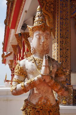 Etkileyici bir Tayland tapınağında heykel sergileniyor. Etrafı karmaşık mimari ve canlı dekorasyonlarla çevrili..