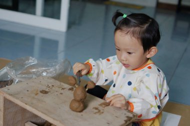 A young child focused on playing with clay, engaged in the process of creation. The child is seated at a wooden table, molding the clay with focus and care