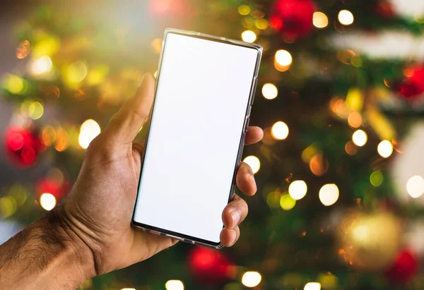 Holding a Mobile On a Christmas Background. Black Hands With Blanck Cell Phone Screen, Space for Text.
