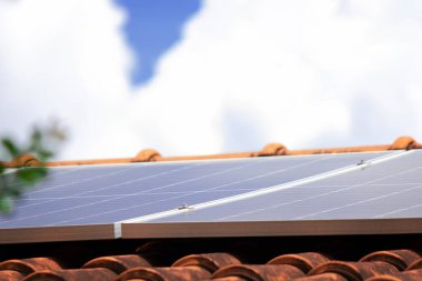 Güneşli ve bulutlu bir günde çatıdaki güneş panelleri. Fotovoltaik Kurulum Etrafında Yapraklar ve Çiçekler Olan Bir Evde.